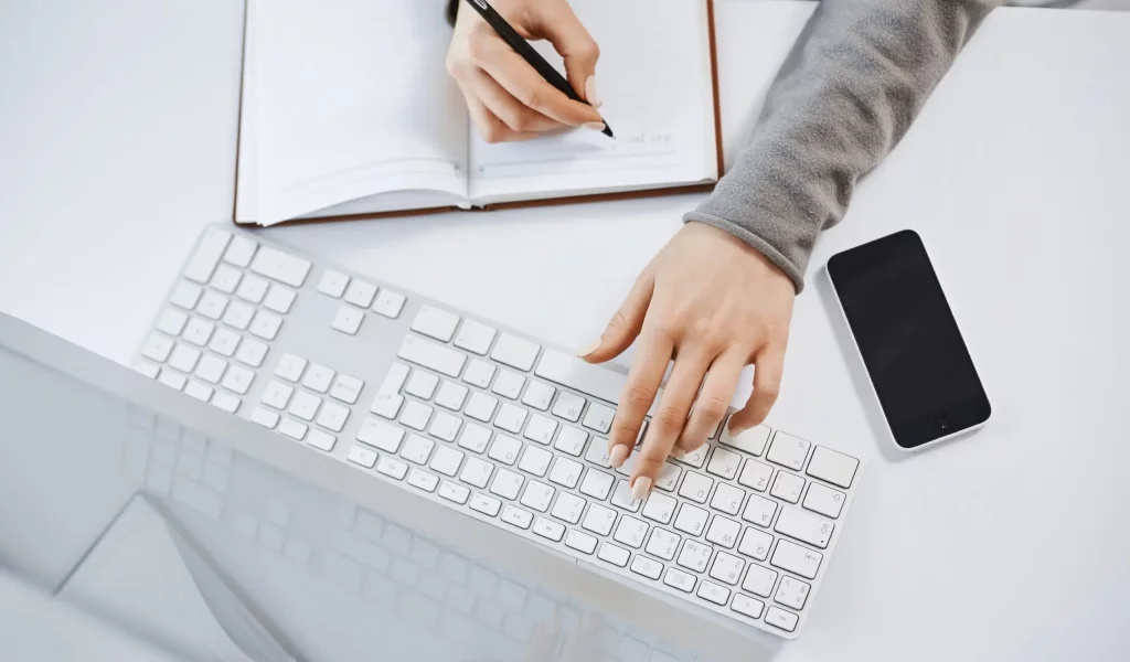 mani di una donna che scrivono su foglio e a computer